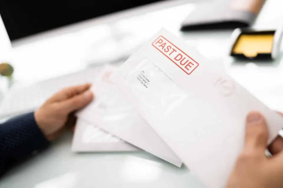 Close-up of hand holding white envelope with red "Past Due" stamp.
